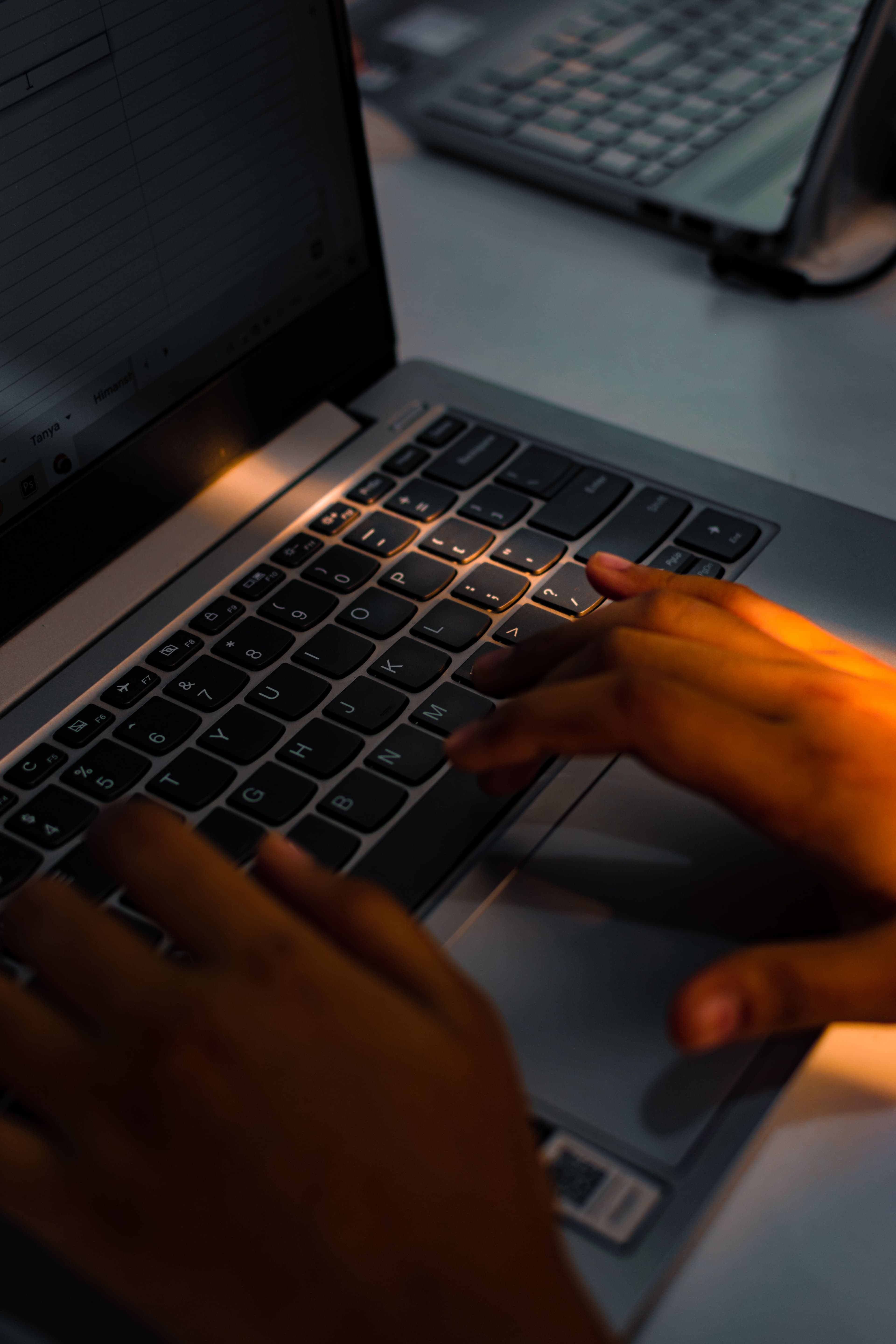 Hands typing on a laptop keyboard in warm light